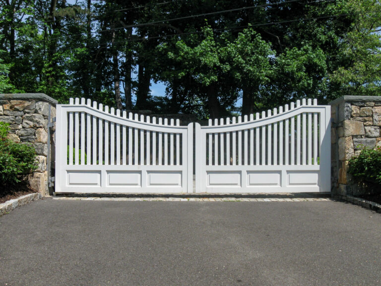 A white composite double gate with a solid lower panel and closely-spaced vertical pickets set between two stone columns.
