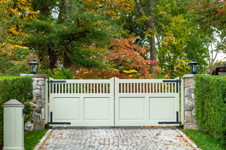 A stone drive leads up to a mostly-solid gray composite double gate with a narrow vertical panel on top.