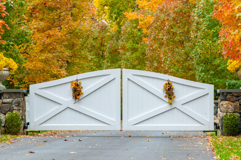 A white composite double gate is reinforced with an x across its two solid panels. Floral decorations hang from the middle of each panel.