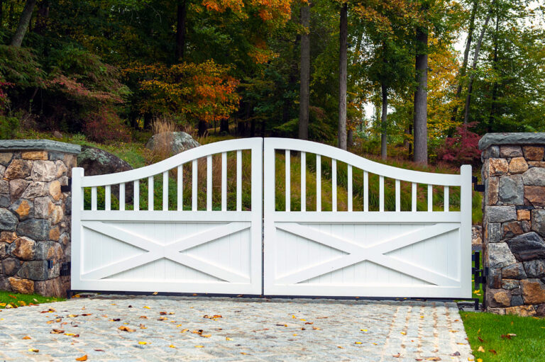 A composite gate painted white has solid panels on the bottom with vertical pickets that curve to reach a gentle apex at the center.