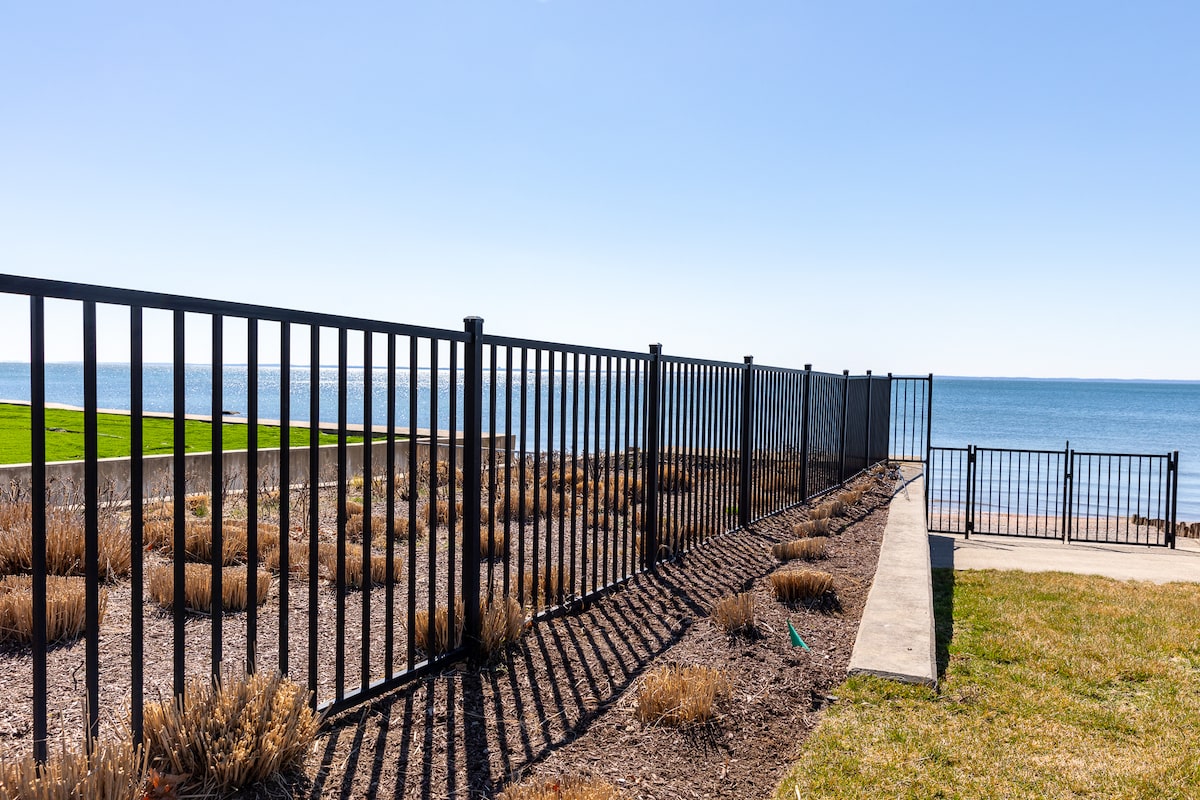 A short black aluminum fence divides two oceanside plots, one with patches of sea grass and lush green lawn.