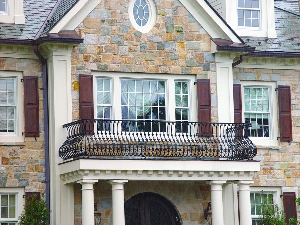 A metal balcony railing with curved vertical railings encloses the second-story window in the center of a home.