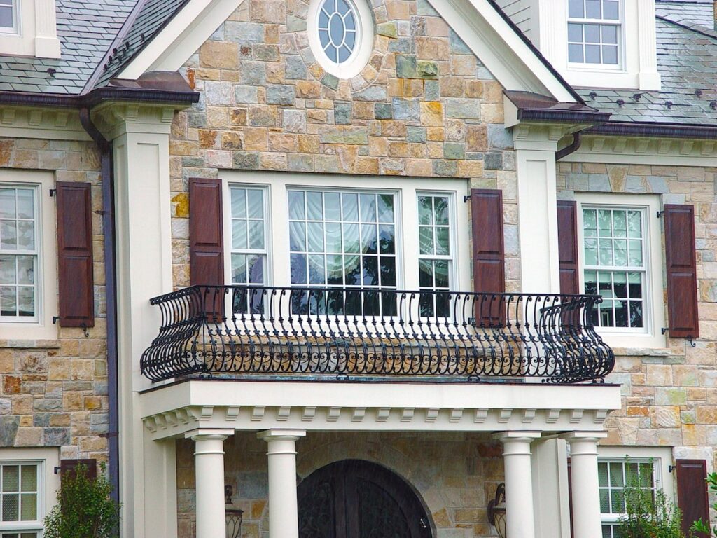 A suburban home with a small black wrought iron balcony with a curved design.
