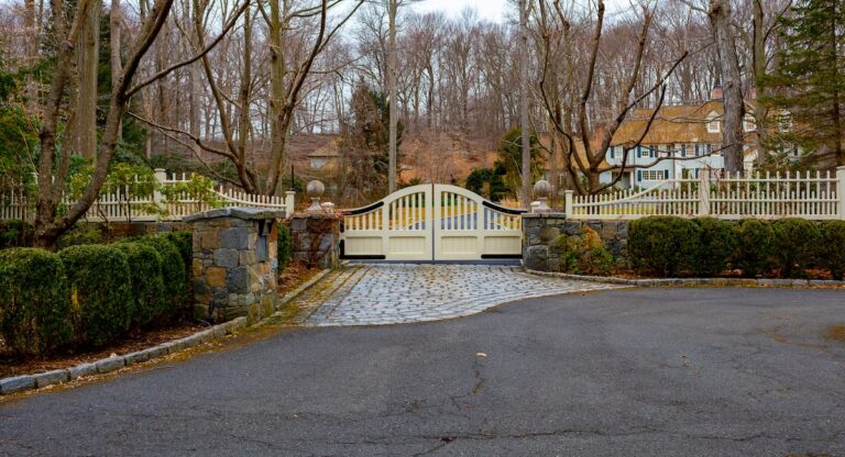 A cream-colored double gate has black steel strap hinges and hangs between two low stone walls.