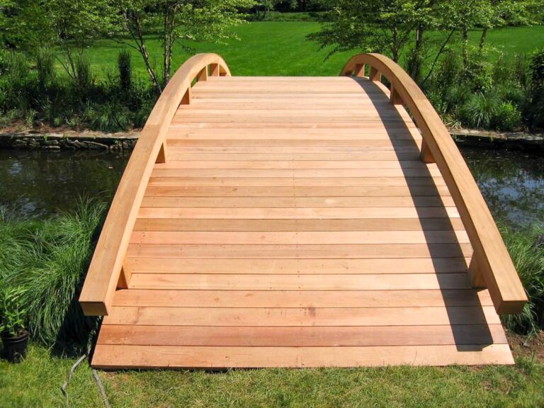 A wide arched garden bridge with a low railing crosses a stream.