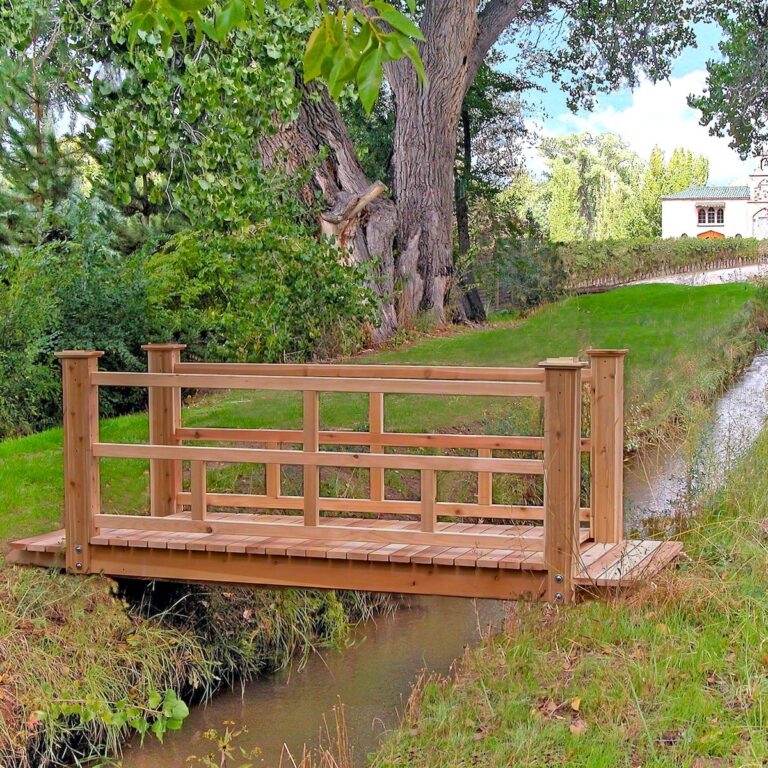 A short, flat, wooden garden bridge with comfortable railings crosses a small creek.