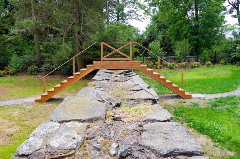 A wooden step bridge leading over a stone wall is pictured in profile.