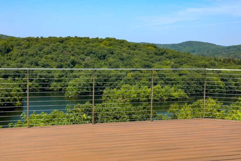 A tall cable rail at the end of a deck allows a clear view of the water, woods, and hills beyond.