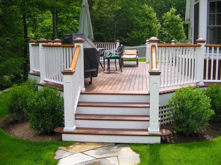 A wooden deck is featured in a backyard surrounded by trees.