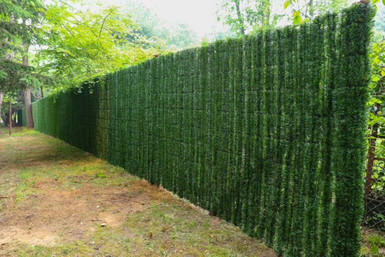 Image shows a long stretch of permanent hedge where green synthetic material is woven through metal mesh to look like an organic hedge.