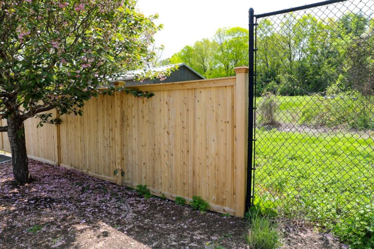 A tall solid 6’ wooden fence is next to an 8’ black metal chain link fence.