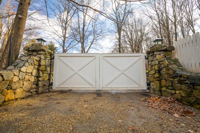 A simple white wood double gate hangs between two stone posts.