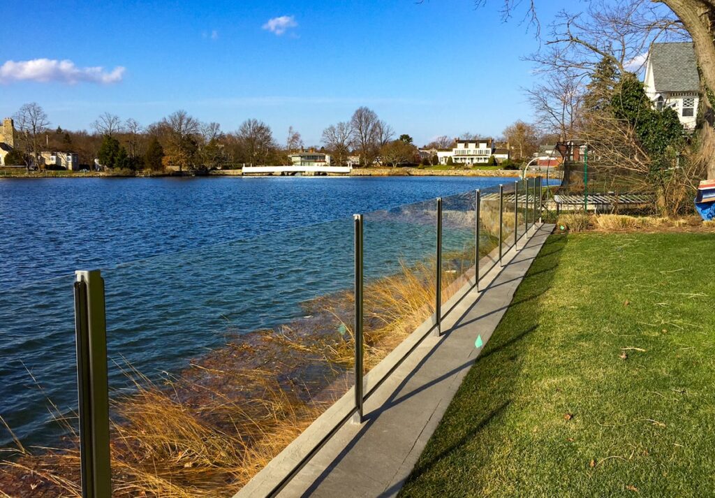 Glass railings separate a backyard from the water’s edge.