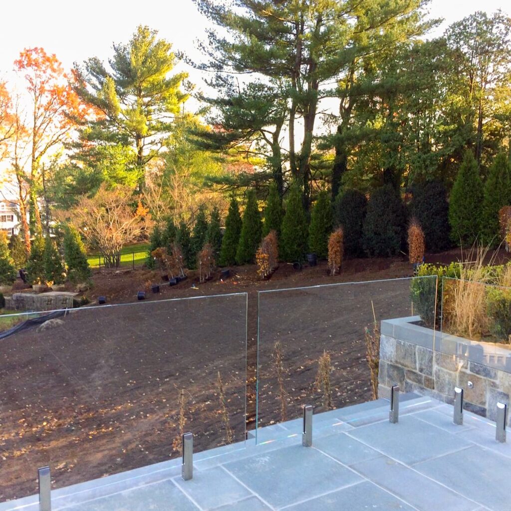 A glass railing separates a slate porch from a wooded area.