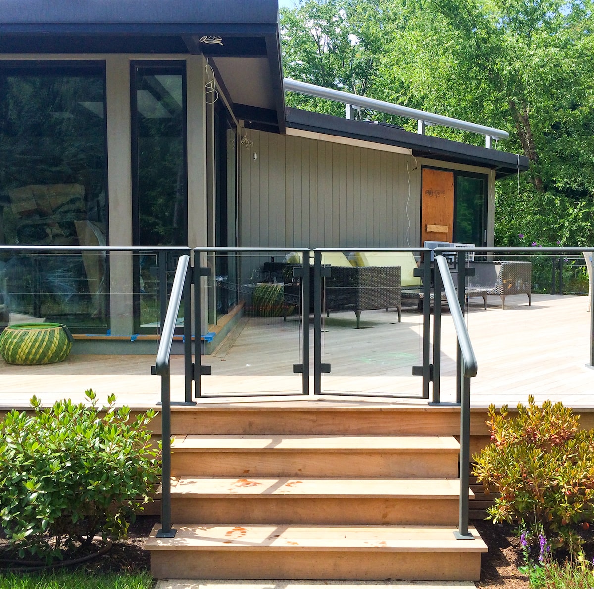 This glass railing has a dark-colored metal frame and features a two-paneled walk gate at the top of the steps.