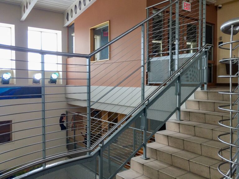 Tall cable rail interior railings run alongside a staircase and around a circular landing. Narrowly-spaced horizontal cable balusters protect visitors from falling.