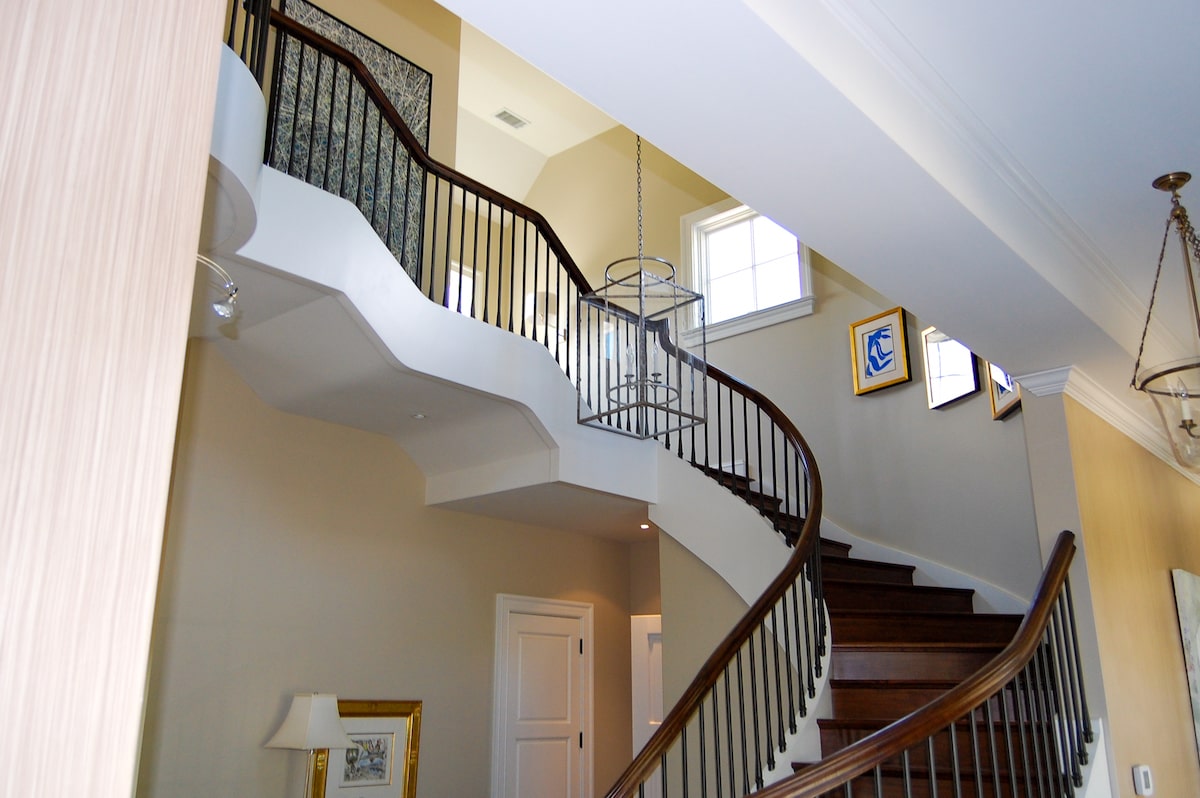 A curved staircase with multiple half landings is flanked by an interior stair railing composed of iron balusters and a dark-stained wood handrail.