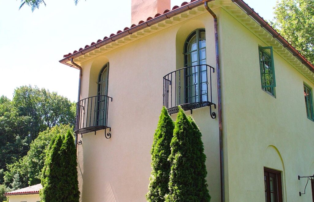 The facade of a home featuring two metal juliet balconies in front of side-by-side second-story arched windows.