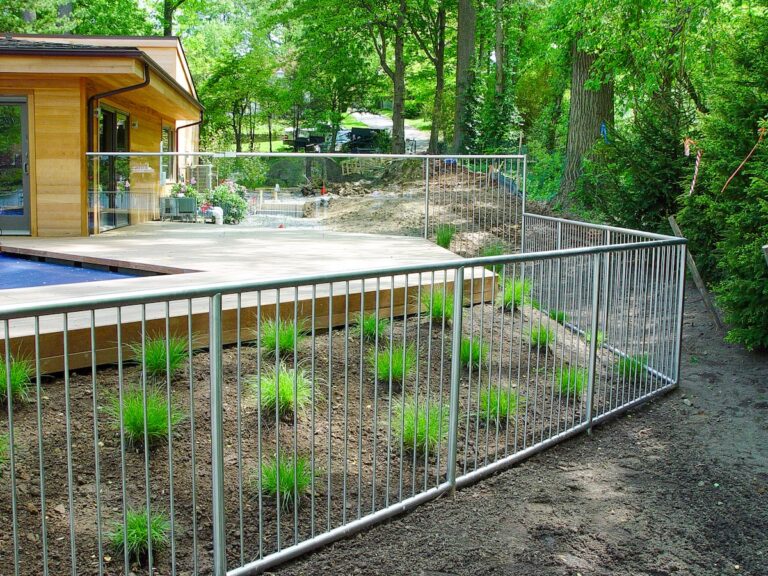 A stainless steel fence with narrow vertical bars surrounds a contemporary in-ground pool; it is sleek and streamlined.