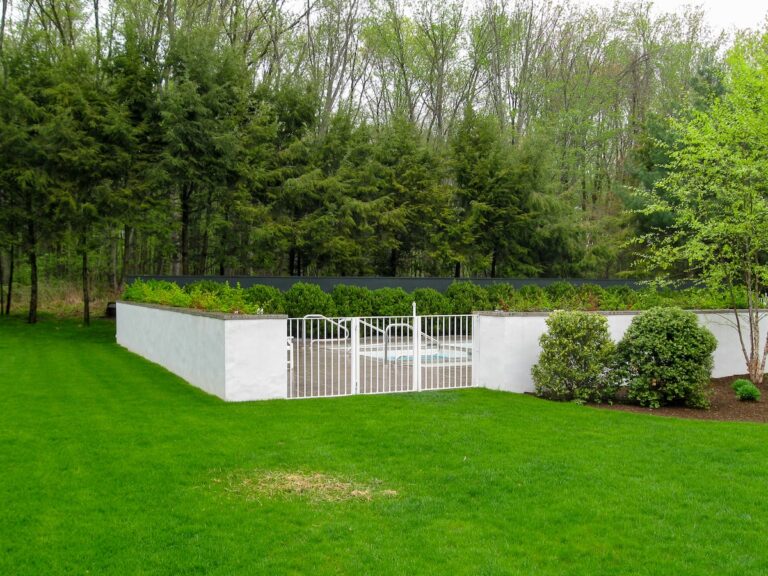 Bright green grass lays between the viewer and a white metal gate set into a whitewashed stone wall.