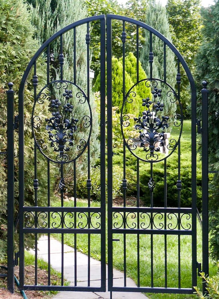A custom wrought iron fence gate with an arch in the middle and handmade inset floral designs.