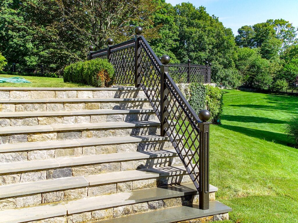 Stone steps with a metal railing with criss-crossed detailwork lead out to a garden.