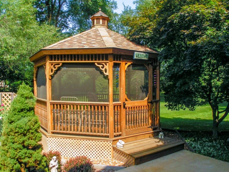 A dark-stained wood gazebo with decorative balusters is placed atop a lattice base. A fine mesh screen along the exterior prevents the space from drawing unwanted insects or animals.