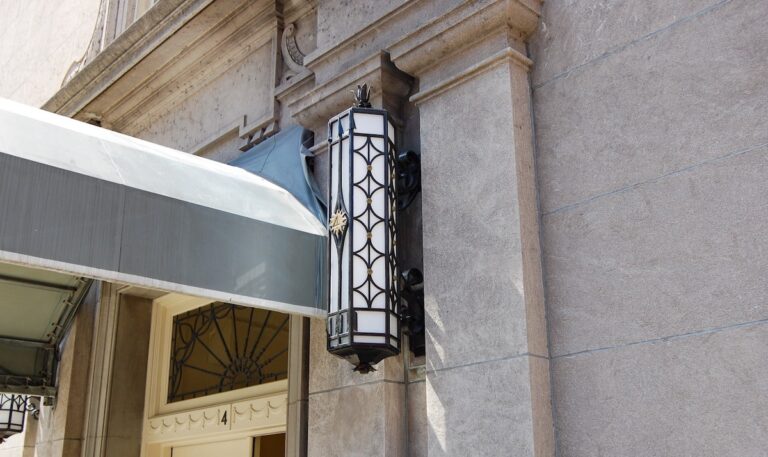 A custom-made decorative exterior sconce made from wrought iron with an Art Deco design extends from a building’s classically-styled limestone facade.