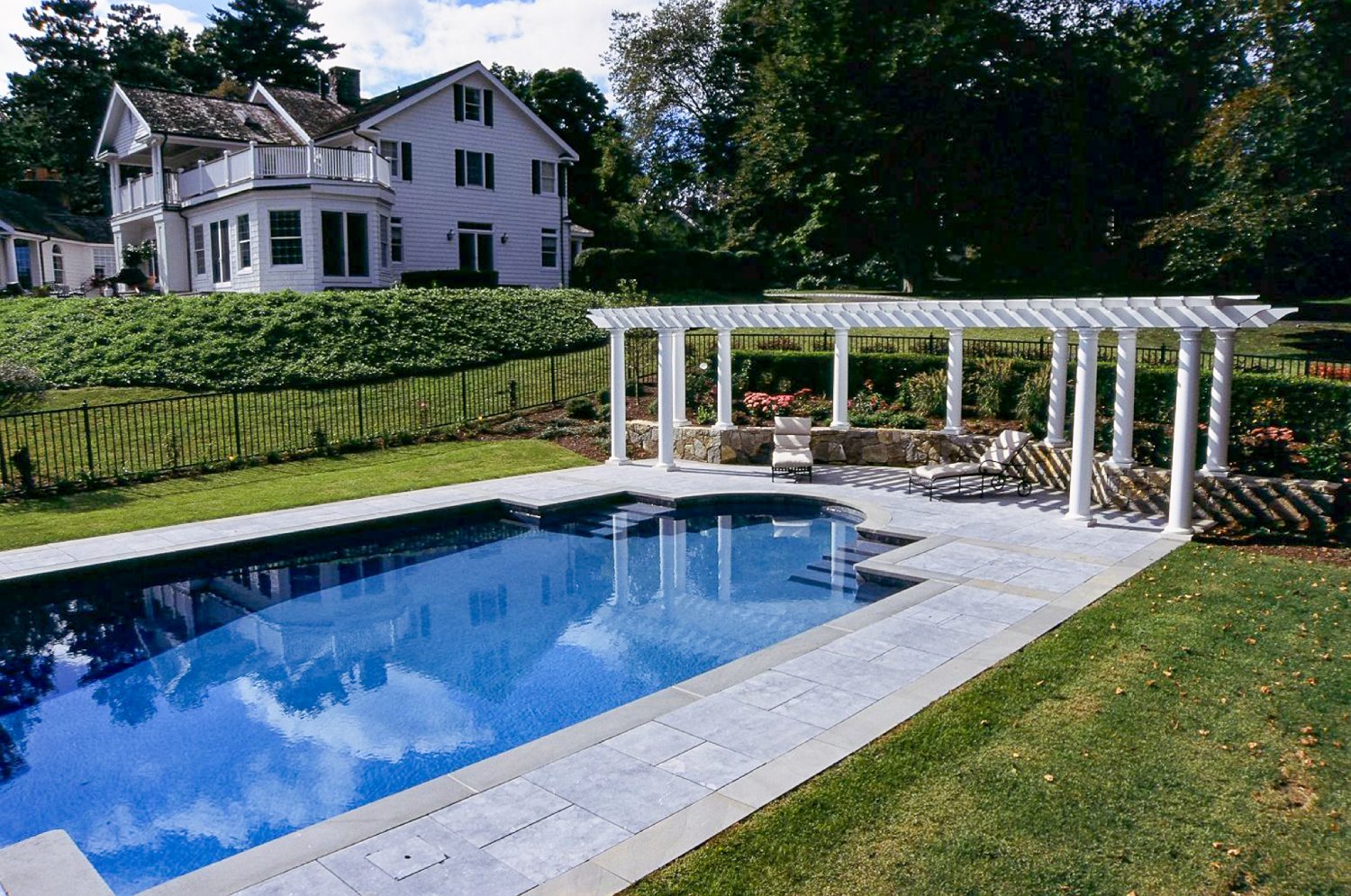 White pergola by the pool with a house on the hill