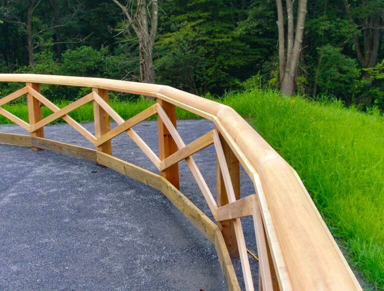 A light wood post and rail fence with diagonal rails positioned in an x pattern curves to form an enclosure.