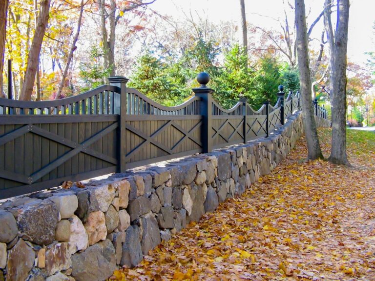 A dark green wood privacy fence with scalloped pickets and alternating decorative post caps atop a stone wall.