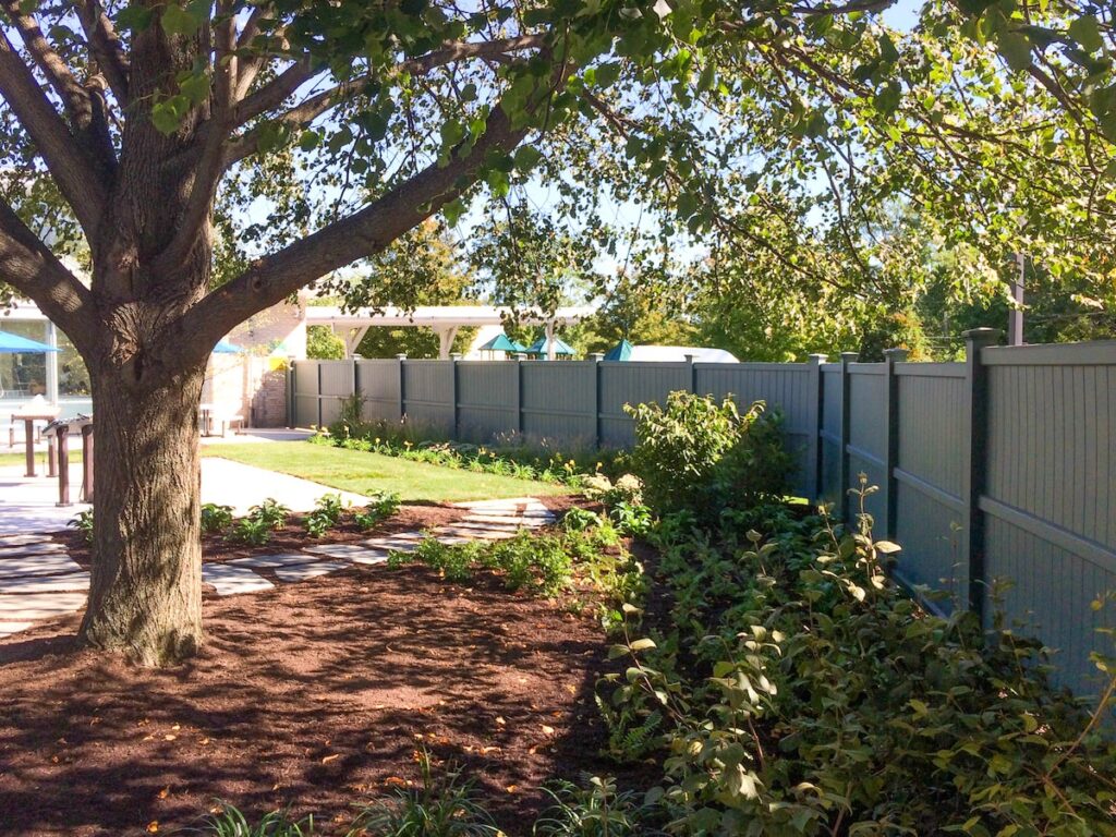 A tall dark gray privacy fence encloses a space with a mature tree.