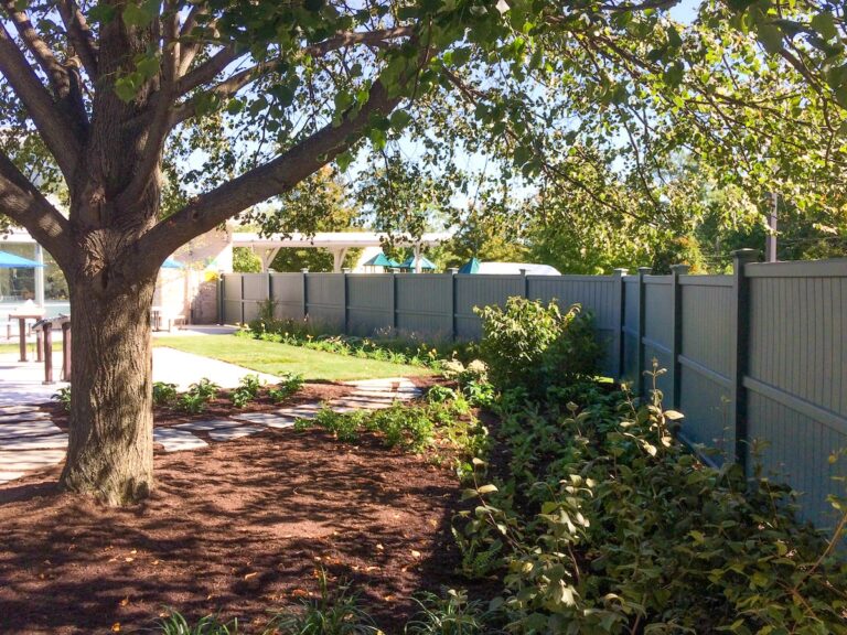 A tall dark gray privacy fence encloses a space with a mature tree.