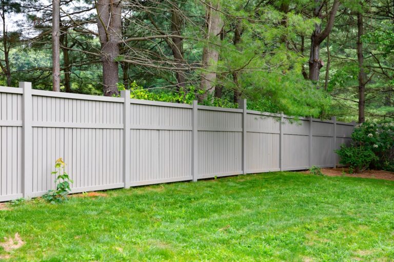a tall gray deer fence divides a lawn from a wooded area.