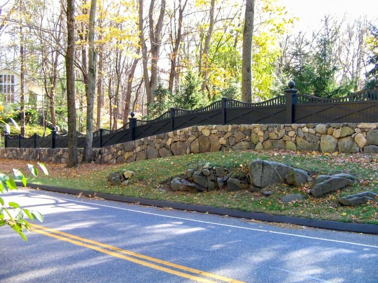A low stone wall is topped with a custom wooden fence featuring a decorative double X design, oversized post and ball details, and a custom radiused top rail.