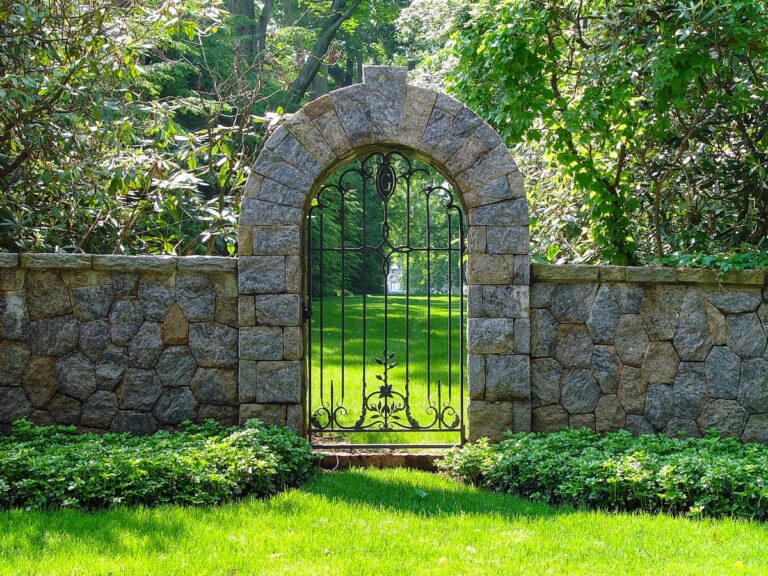 A stone archway is inset in a low stone wall. There is a wrought iron gate in the archway.
