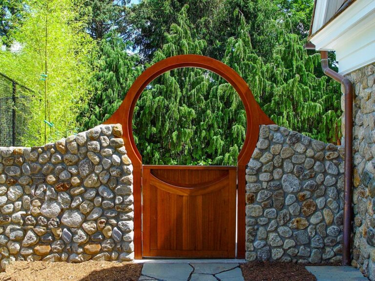 A stone wall rises gently to meet a wooden archway and gate set into the wall.