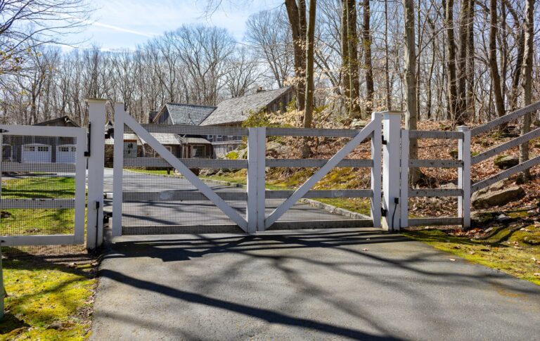 A simple white post and rail gate sits between a post and rail fence.