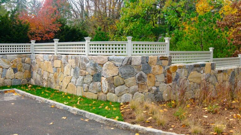 A dry-fit stone wall is topped with narrow white lattice panels custom shaped to match the wall’s curvature.