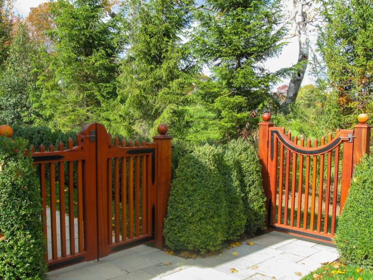 Two dark-stained mahogany fence gates, one with two panels, the other with one, lead to separate parts of a garden.