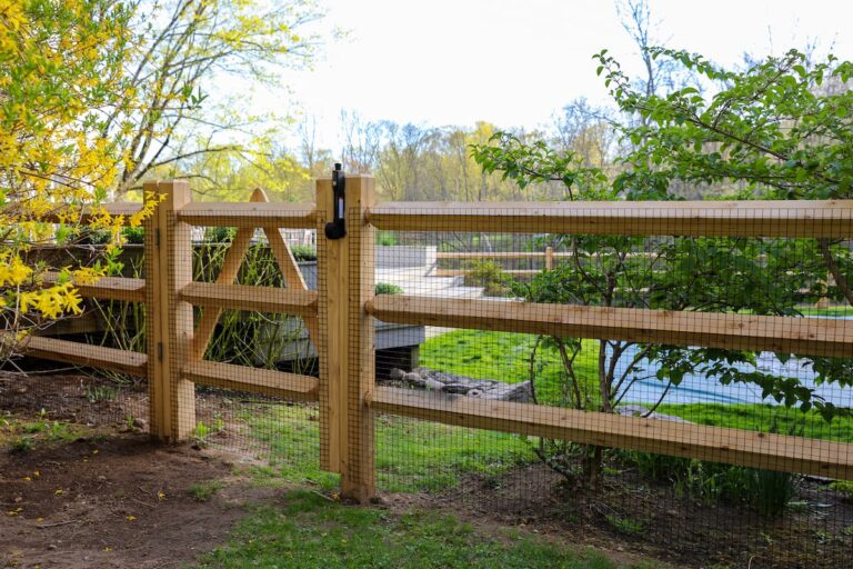 A wood fence gate leads through a split rail fence to a covered pool.
