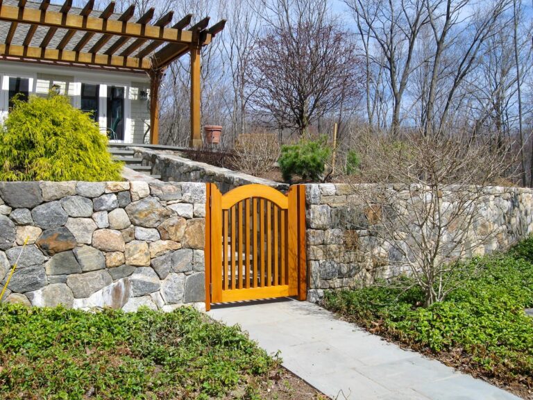 A wood fence gate set in a low stone wall leads to steps up the back deck.
