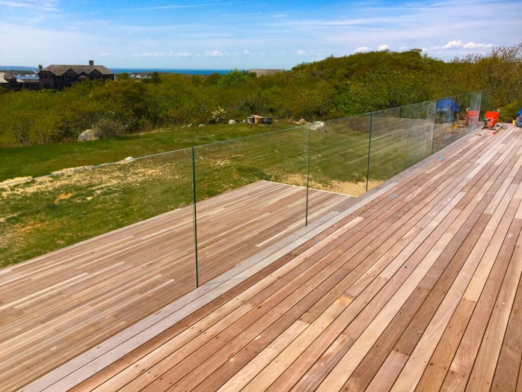 A clear glass railing on a wood deck offers an unobstructed view of a grassy treelawn.