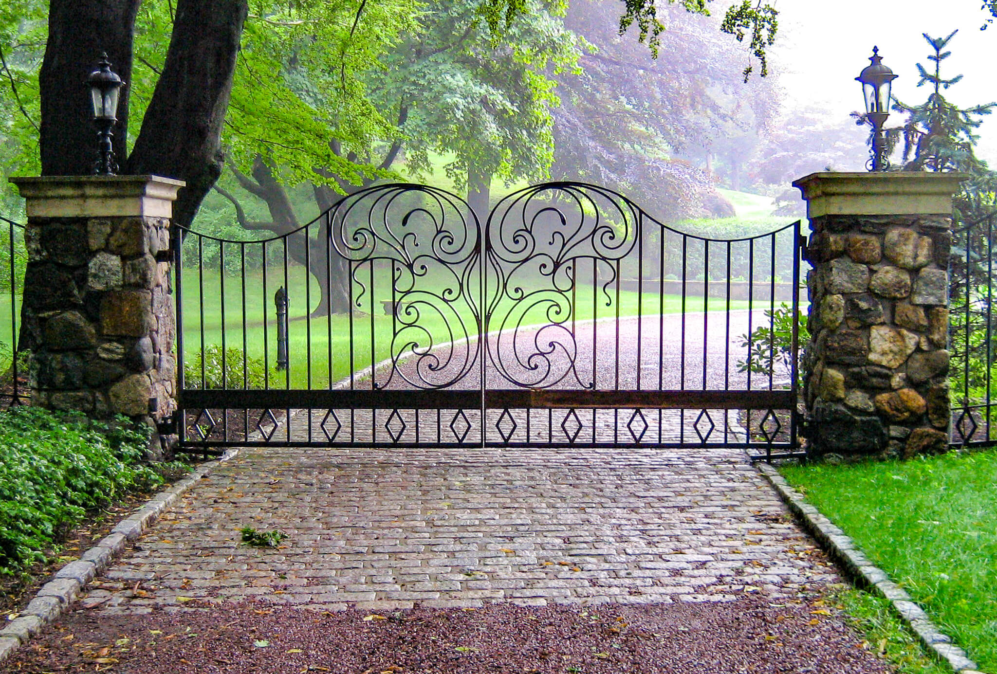 wrought iron driveway gate with elaborate scrollwork installed on two stone pillars
