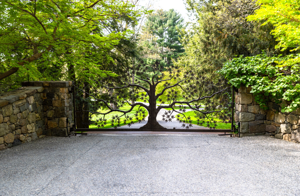 Custom wrought-iron driveway gate with a tree-branch design set between stone columns