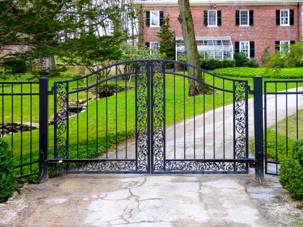 Ornate wrought-iron double driveway gate with scrollwork before a brick estate