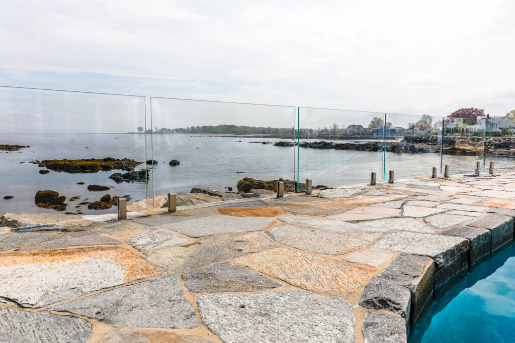 Frameless glass railing on a coastal stone patio overlooking the water