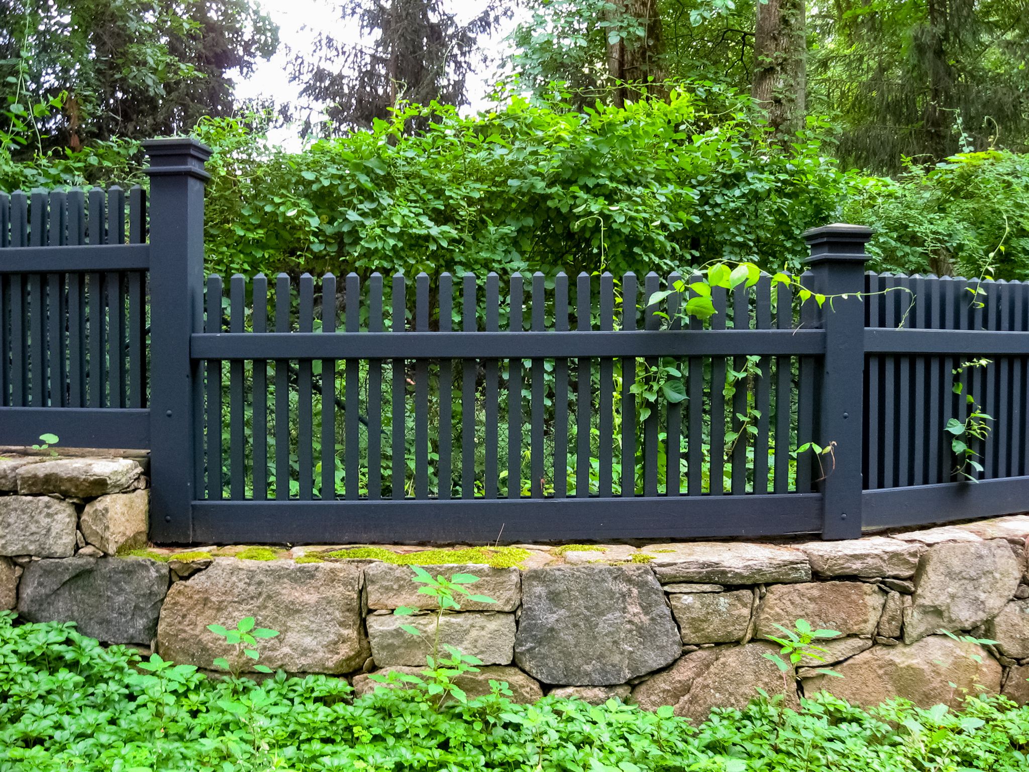 Deceptively composite fence built on a stonewall amid green groundcover and bushes